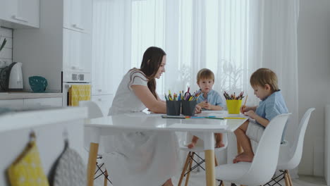 Zwei-Kinder-Eines-Jungen-Zeichnen-Mit-Seiner-Mutter,-Die-In-Der-Küche-Sitzt.